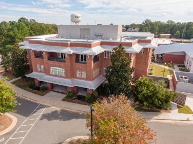 Kuzey Carolina 'daki Apex Town Hall' un hava aracı görüntüsü. Beyaz mimari çerçeveli çok katlı kırmızı tuğlalı belediye binası. Çekim çatıdaki mekanik çatı katı ve arka plandaki 