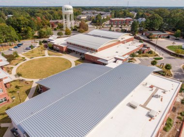 Yüksek açılı hava manzarası, NC 'nin Apex kentindeki modern bir belediye binasının geniş, ayakta duran metal çatısını vurguluyor. Gri tırtıklı paneller, bitişik tuğla duvarlar ve dairesel çimlerle çelişen ana yapıyı kaplıyor..