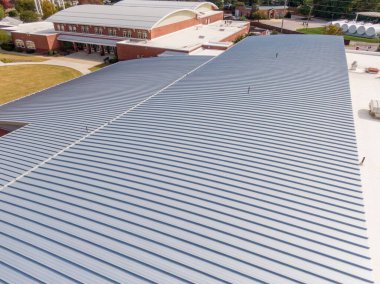 Yüksek açılı hava manzarası, NC 'nin Apex kentindeki modern bir belediye binasının geniş, ayakta duran metal çatısını vurguluyor. Gri tırtıklı paneller, bitişik tuğla duvarlar ve dairesel çimlerle çelişen ana yapıyı kaplıyor..