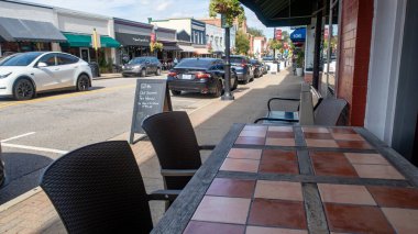 Apex, NC 'deki beton kaldırımda alçak açılı, sokak seviyesinde bir çekim. Gümüş renkli metal bir köpek kasesi, park halindeki arabaların ve tarihi mağazaların bulunduğu siyah bir elektrik direğinin yanında, mavi gökyüzünün altında arka planda duruyor..