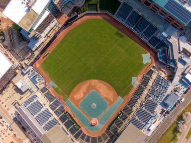 Güneşli bir öğleden sonra Durham Bulls Atletizm Parkı 'nda tepeden tırnağa havalandı. Çekimde yeşil çimenler, toprak taban yolları ve elması kaplayan koyu mavi stadyumla çevrili mavi bir branda yer alıyor..