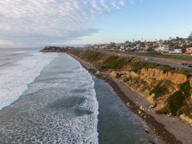 Güney Kaliforniya 'daki Encinitas sahil şeridine geniş bir hava manzarası. Görüntü, kumlu kıyıya yuvarlanan beyaz dalgaları, dik sahil kayalıkları ve Pasifik Okyanusu 'na bakan araçların park ettiği manzaralı bir gözcüyü yakalıyor..