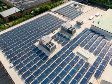 Endüstriyel düz bir çatıdaki devasa bir güneş panelinin xpansive görüntüsü. Yüksek açılı görüntü, HVAC birimleri, tavan pencereleri ve yeşil enerji altyapısını vurgulayan bir park alanı ile birlikte birçok sıra mavi fotovoltaik modül yakalar..