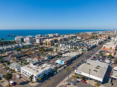Oceanside şehir merkezinin Pasifik 'e bakan yüksek açılı hava manzarası. Görüntü şehrin sokaklarını, renkli duvar resimlerini ve kıyıya uzanan palmiye ağaçlarını gösteriyor. İkonik rıhtım ve mavi ufuk uzaklıktan görülebiliyor..