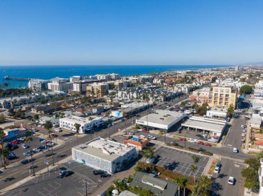 A high-angle aerial view of downtown Oceanside looking toward the Pacific. The image shows city streets, colorful murals, and palm trees leading to the coastline, with the iconic pier and blue horizon visible in the distance.