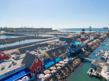 Okyanus Kıyısı Köyü 'ne bakan bir hava manzarası. Kırmızı ve beyaz deniz feneri deniz kenarında, deniz kenarındaki dükkanların yanında ve bir köprünün yanında duruyor. Pasifik kıyı şeridi ve parlak, berrak bir ufuk uzaklıktan görülebilir..