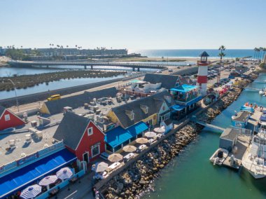 Okyanus Kıyısı Köyü 'ne bakan bir hava manzarası. Kırmızı ve beyaz deniz feneri deniz kenarında, deniz kenarındaki dükkanların yanında ve bir köprünün yanında duruyor. Pasifik kıyı şeridi ve parlak, berrak bir ufuk uzaklıktan görülebilir..