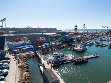 Hava manzarası büyüleyici Oceanside Liman Köyü 'nü gösteriyor. Kırmızı ve beyaz çizgili deniz feneri renkli rıhtım dükkanları ve 
