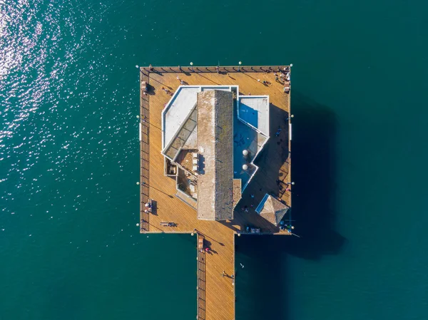 Yangından önce California 'daki ikonik Oceanside Rıhtımı' nın yukarıdan aşağıya muhteşem manzarası. Ahşap güverte ve merkez bina derin Pasifik Okyanusu üzerinde mükemmel bir şekilde merkezlenmiştir. Güneş ışığı suyun yüzeyinden yansımaktadır..