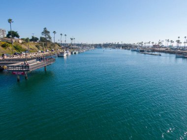 Oceanside Limanı 'nın ana kanalına bakan bir hava manzarası. Ön planda bir kürekçi, kenetlenmiş yelkenliler ve hareket halindeki birkaç küçük motorlu botla çevrili derin mavi sularda gezinirken kameraya el sallıyor..
