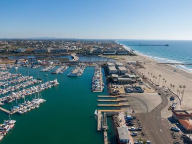 Okyanus kıyısındaki panorama yelkenli ve yatlarla dolu. Manzarada limanın sakin turkuaz suyu, ikonik deniz feneri ve uzaktaki Oceanside İskelesi ile San Luis Rey Nehri 'ni geçen bir köprü yer alıyor..