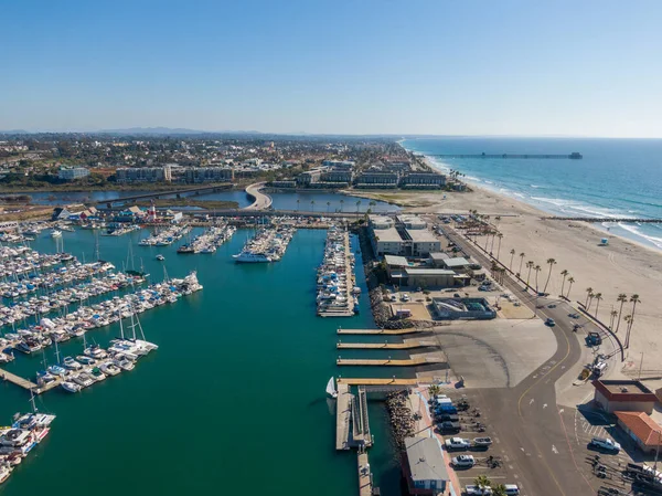 Okyanus kıyısındaki panorama yelkenli ve yatlarla dolu. Manzarada limanın sakin turkuaz suyu, ikonik deniz feneri ve uzaktaki Oceanside İskelesi ile San Luis Rey Nehri 'ni geçen bir köprü yer alıyor..