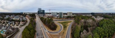 Raleigh 'deki North Hills siluetini yakalayan panoramik bir hava görüntüsünde yüksek katlı karma kullanım kuleleri ve etkin inşaat alanları yer alıyor. I-440 Beltline, yerleşim bölgeleri ve yemyeşil orman bölgeleriyle sınırlandırılmış, arazi boyunca kıvrımlar çizer.