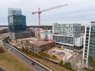 Yüksek açılı bir hava perspektifi, Raleigh 'in North Hills bölgesindeki bir inşaat alanını yakalıyor. Park Central apartmanının bitişiğindeki çok katlı beton bir otoparkın üzerinde uzun kırmızı bir vinç duruyor..