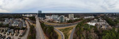 Raleigh 'deki North Hills siluetini yakalayan panoramik bir hava görüntüsünde yüksek katlı karma kullanım kuleleri ve etkin inşaat alanları yer alıyor. I-440 Beltline, yerleşim bölgeleri ve yemyeşil orman bölgeleriyle sınırlandırılmış, arazi boyunca kıvrımlar çizer.