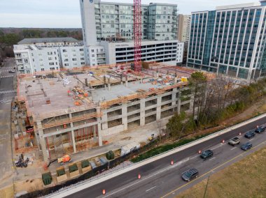 Yüksek açılı bir hava perspektifi, Raleigh 'in North Hills bölgesindeki bir inşaat alanını yakalıyor. Park Central apartmanının bitişiğindeki çok katlı beton bir otoparkın üzerinde uzun kırmızı bir vinç duruyor..