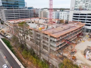 Yüksek açılı bir hava perspektifi, Raleigh 'in North Hills bölgesindeki bir inşaat alanını yakalıyor. Park Central apartmanının bitişiğindeki çok katlı beton bir otoparkın üzerinde uzun kırmızı bir vinç duruyor..