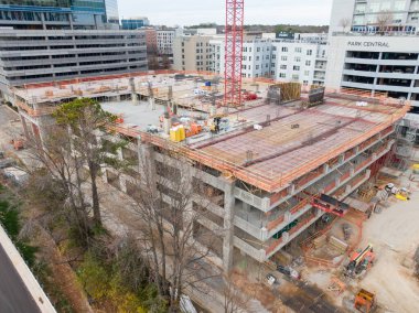 Yüksek açılı bir hava perspektifi, Raleigh 'in North Hills bölgesindeki bir inşaat alanını yakalıyor. Park Central apartmanının bitişiğindeki çok katlı beton bir otoparkın üzerinde uzun kırmızı bir vinç duruyor..