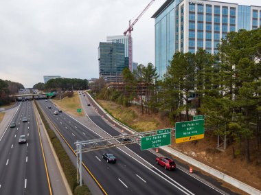 Geniş açılı insansız hava aracı Raleigh 'in North Hills bölgesindeki Six Forks Road kavşağında I-440 Beltline gösteriyor. Çekim, yüksek binalar, etkin inşaat vinçleri ve otoyolda uzanan yeşil çam ağaçlarını yakalıyor..