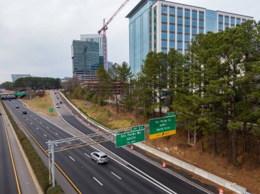 Geniş açılı insansız hava aracı Raleigh 'in North Hills bölgesindeki Six Forks Road kavşağında I-440 Beltline gösteriyor. Çekim, yüksek binalar, etkin inşaat vinçleri ve otoyolda uzanan yeşil çam ağaçlarını yakalıyor..