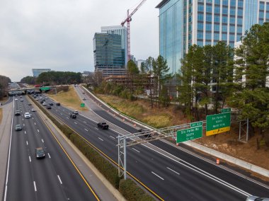 Geniş açılı insansız hava aracı Raleigh 'in North Hills bölgesindeki Six Forks Road kavşağında I-440 Beltline gösteriyor. Çekim, yüksek binalar, etkin inşaat vinçleri ve otoyolda uzanan yeşil çam ağaçlarını yakalıyor..