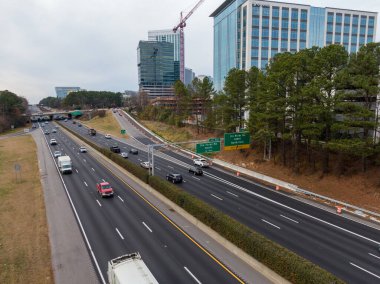 Geniş açılı insansız hava aracı Raleigh 'in North Hills bölgesindeki Six Forks Road kavşağında I-440 Beltline gösteriyor. Çekim, yüksek binalar, etkin inşaat vinçleri ve otoyolda uzanan yeşil çam ağaçlarını yakalıyor..