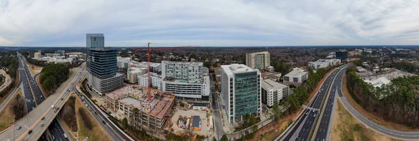 Raleigh 'deki North Hills siluetini yakalayan panoramik bir hava görüntüsünde yüksek katlı karma kullanım kuleleri ve etkin inşaat alanları yer alıyor. I-440 Beltline, yerleşim bölgeleri ve yemyeşil orman bölgeleriyle sınırlandırılmış, arazi boyunca kıvrımlar çizer.