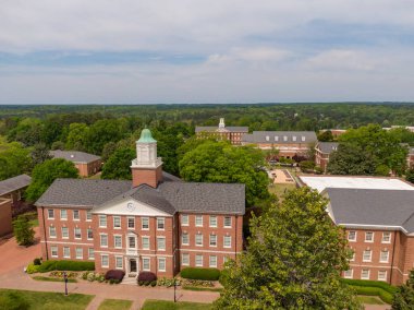 Wake Forest, NC 'deki tarihi tuğla kampüsünün geniş kapsamlı bir antresi. Görüntü, mimari kiremitleri, bakır kubbeli kubbeleri ve simetrik duvarları olan geniş katlı çatıları vurguluyor ve geleneksel kurumsal yapı tasarımını gösteriyor.