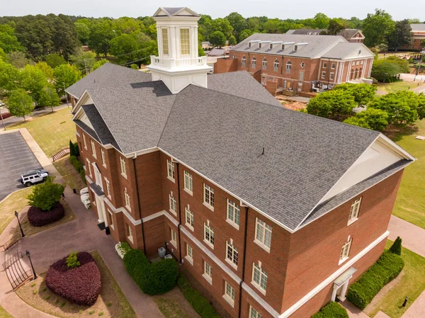 Wake Forest, NC 'deki tuğla bir kurumsal binanın detaylı hava görüntüsü. Bu 2026 görüntüsünde belirgin beyaz kubbe, çoklu çember ve hassas sırt kaplamalı karmaşık mimari bir çatı sistemi sergilenmektedir..