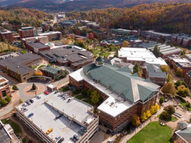 Yüksek açılı insansız hava aracı Boone şehir merkezindeki büyük bir ticari bina ve park yerine bakıyor. Şehrin mimarisi, sonbahar yapraklarıyla kaplı, yuvarlanan Appalachian tepelerine dayanır..