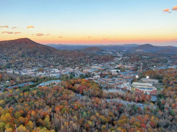 Geniş bir hava manzarası, sonbaharda Blue Ridge Dağları 'nın kayan tepelerini yakalar. Boone kasabası, yumuşak bir alacakaranlık gökyüzünün altında, turuncu ve altın yeşilliklerden oluşan canlı bir duvar halısı ile çevrili, vadide yuva kurmuştur..