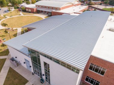 Yüksek açılı hava manzarası modern endüstriyel ayakta dikilen metal çatıyı gösteriyor. Gıcır gıcır, doğrusal kaburgalar ve slate-gray kaplama profesyonel kurulum, dayanıklılık ve ticari veya ikamet kullanımı için çağdaş mimari stili vurgular.