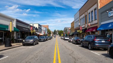 Kuzey Salem Caddesi 'nden Kuzey Carolina, Apex' in tarihi kalbine doğru bakan zemin seviyesinde, göz hizasında bir perspektif. Çekim, kasabanın küçük kasaba cazibesini, paralel park etmiş arabaları, tuğla dükkanları ve açık mavi gökyüzü ile yakalıyor..