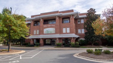 Kuzey Carolina 'daki Apex Town Hall' un kırmızı tuğlalı dış görüntüsü. Binanın geniş pencereleri, beyaz mimari çerçevesi ve yeşil peyzajı, toplumun idari kalbini temsil ediyor..