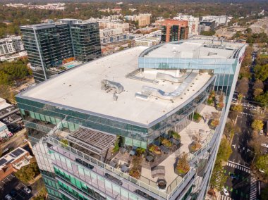 Beyaz bir TPO zarı, karmaşık bir HVAC kanalı ve oturma ve saksıları olan lüks bir terası olan modern yüksek katlı bir çatı katının insansız hava aracı görüntüsü. Bu çekim endüstriyel araç ve üst düzey şehir mimarisinin kesişimine vurgu yapıyor..