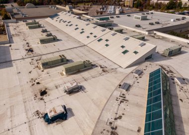 Geniş beyaz halka arz ticari çatısının yüksek açılı görüntüsü. Çok sayıda küçük cam paneller, çoklu büyük HVAC birimleri ve koyu gölgelik ve enkazları gösteren birkaç düz çatı bölgeleri ile büyük, eğimli bir çatı penceresi bölümü yer almaktadır..