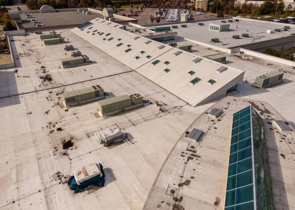 Geniş beyaz halka arz ticari çatısının yüksek açılı görüntüsü. Çok sayıda küçük cam paneller, çoklu büyük HVAC birimleri ve koyu gölgelik ve enkazları gösteren birkaç düz çatı bölgeleri ile büyük, eğimli bir çatı penceresi bölümü yer almaktadır..