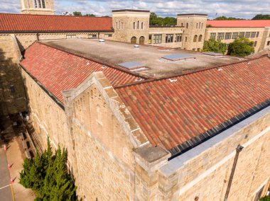 Yüksek açılı hava aracı görüntüsü, taş akademik bir binada kırmızı kil kiremit bir çatı gösteriyor. Yapıda düz bir bölümde geniş çatı pencereleri ve tarihi taş ve oluklarla birlikte entegre metal oluklar yer alıyor..