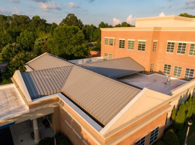 Bu hava aracı görüntüsünde bronzlaşmış, ayakta duran metal bir çatı klasik bir tuğla binayla buluşuyor. Yüksek açılı çekim, hassas doğrusal dikişler ve yıldırım koruma çubukları yakalar, profesyonel mimari metalleri vurgular ve dayanıklı koruma sağlar.