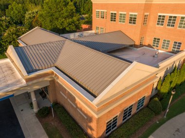 Bu hava aracı görüntüsünde bronzlaşmış, ayakta duran metal bir çatı klasik bir tuğla binayla buluşuyor. Yüksek açılı çekim, hassas doğrusal dikişler ve yıldırım koruma çubukları yakalar, profesyonel mimari metalleri vurgular ve dayanıklı koruma sağlar.