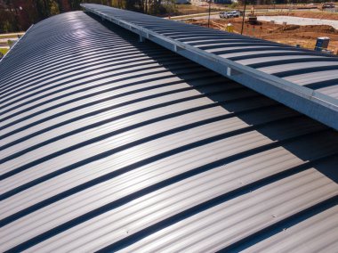 Bu hava aracı görüntüsünde modern bir ticari binanın gri, ayakta duran metal bir çatısı görülüyor. Temiz doğrusal tasarım ve entegre oluk sistemi, üst düzey perakende sahaları için profesyonel kurulum ve kalıcı mimari korumayı vurguluyor.