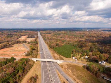 Bu hava görüntüsü, Kuzey Carolina 'daki Johnston County kırsalından geçen 40 numaralı otobanı gösteriyor. Karayolu, açık bir sonbahar öğleden sonrası boyunca açık ve parlak, parçalı bulutlu bir gökyüzü altında yoğun sonbahar ormanları ve açık tarım arazileriyle çevrelenmiştir..