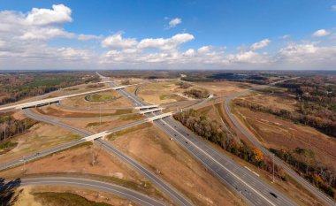 Bu hava çekimi Kuzey Carolina, Raleigh yakınlarındaki 40 numaralı otoban otobanındaki karmaşık türbin kavşağını gösteriyor. Karmaşık yol sistemi verimli Piedmont ormanları boyunca dokumakta, modern altyapıyı, yoğun trafiği ve bölgenin geniş çapını gözler önüne sermektedir..