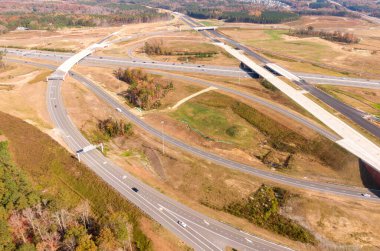 This aerial shot captures the complex turbine interchange on Interstate 40 near Raleigh, North Carolina. The intricate road system weaves through lush Piedmont forests, showcasing modern infrastructure, heavy traffic, and the vast scale of the area.
