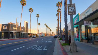 Tarihi bir Kaliforniya 101 tabelası Oceanside 'da palmiye çizgili bir caddede duruyor. Altın saat ışığı, gün batımında bu ikonik otoyolun klasik Güney Kaliforniya kıyı atmosferini yakalayarak yerel mağazalara ve Full Lane yol işaretlerine vuruyor..