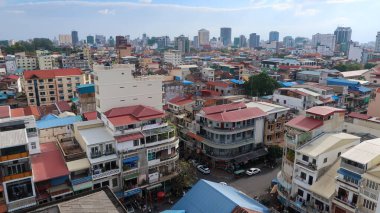 Phnom Penh 'in geniş bir hava manzarası, orta katlı daireler ve geleneksel kırmızı çatılı binaların yoğun bir karışımını gösteriyor. Modern gökdelenler mavi gökyüzünün altında yükselerek, Kamboçya 'nın başkentinin hızlı kentsel gelişimini resmediyor..