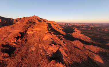 Batıl inanç Dağları 'nın güneş doğarken koyu turuncu ışıkta parlayan hava manzarası. Sivri volkanik tepeler, engebeli Arizona manzarası boyunca uzun gölgeler bırakır. Altın Kanyon 'daki ikonik Sonor Çölünün manzaralı bir perspektifi..