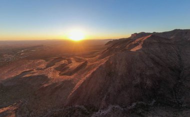 AZ 'deki Altın Kanyon' daki Batıl inanç Dağları 'nın üzerinden yükselen güneşin insansız hava aracı görüntüsü. Altın ışık, Sonoran Çölü 'nün engebeli tepelerine ve derin kanyonlarına vurur. Arizona 'nın vahşi doğası ve dağ ufkunun nefes kesici sabah manzarası..