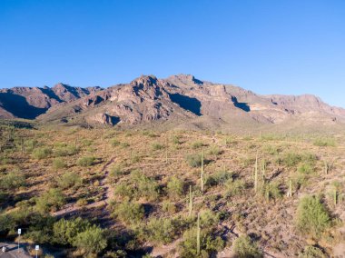 Arizona 'daki Altın Kanyon' daki engebeli Batıl inanç Dağları 'nın insansız hava aracı görüntüsü. Öğleden sonra ışığı, uçsuz bucaksız Sonoran Çölü manzarasını aydınlatıyor. Dönen yürüyüş yollarını ve dağılmış saguaro kaktüslerini gösteriyor. Devasa kaya tepelerine doğru gidiyor..