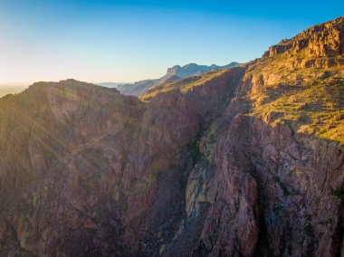 Arizona 'daki Altın Kanyon' daki Batıl inanç Dağları 'nda güneşin batışını gösteren hava aracı görüntüsü. Ufukta parlak güneş ışıkları parlıyor, engebeli çöl uçurumlarını aydınlatıyor ve Sonora 'nın engin manzarasını sıcak, altın saatli bir parıltıyla aydınlatıyor..